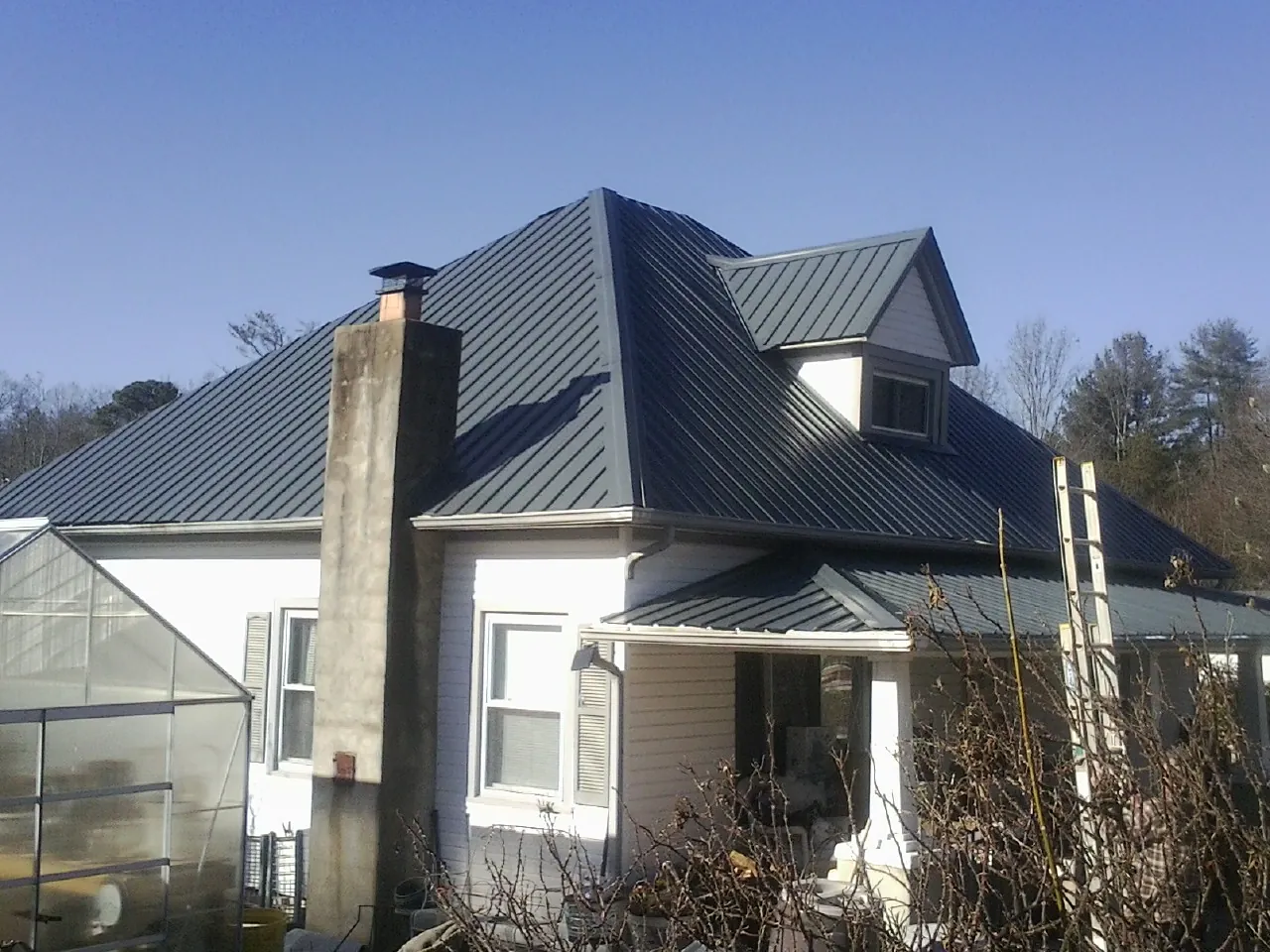 Dark blue standing seam metal roof on a white farmhouse with dormer — Slate & Tile Roof Repair by Roofing Brothers in Broadview