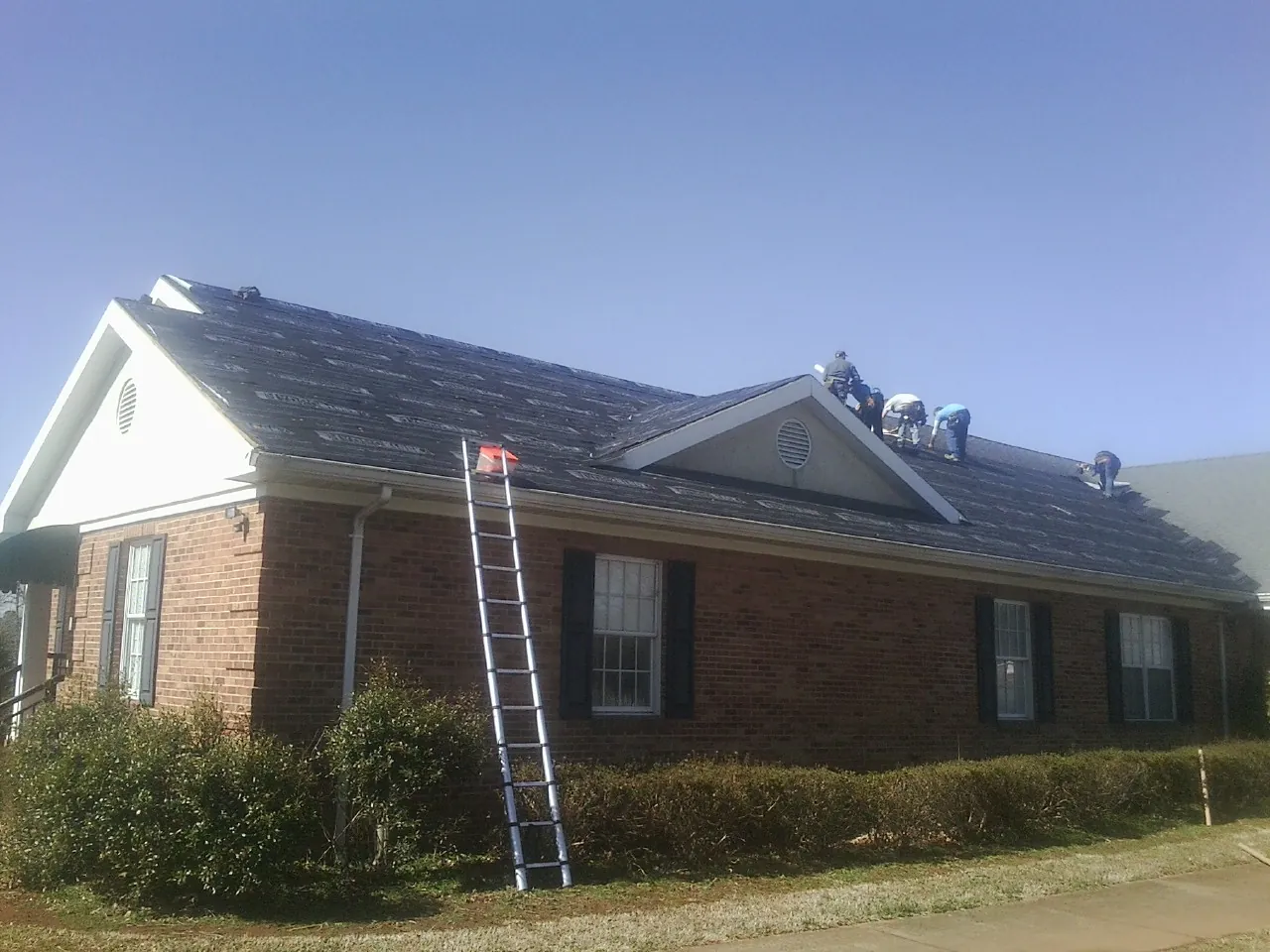 Crew tearing shingles off a brick ranch roof with a ladder set — Metal Roof Repair work by our crew in Broadview
