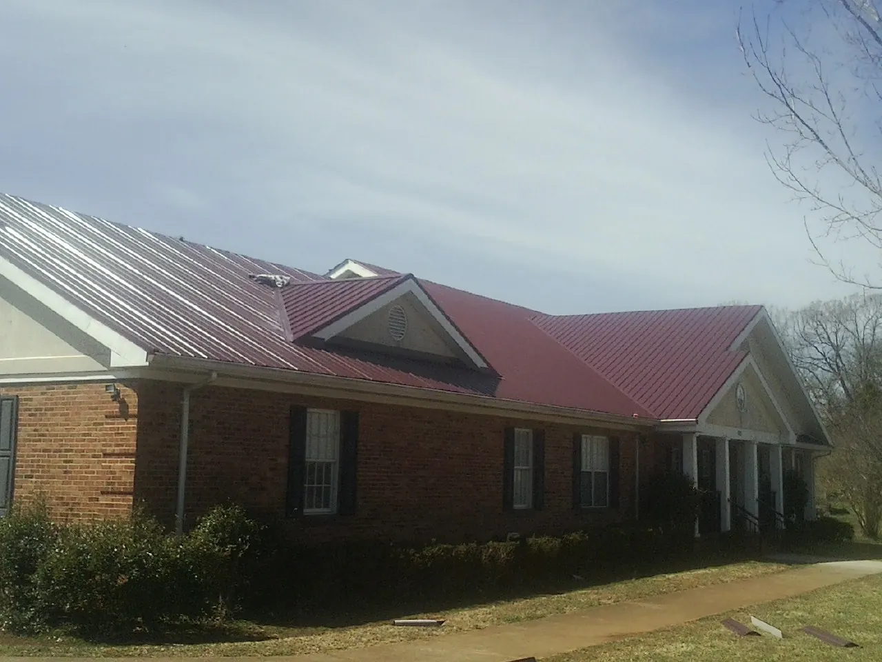 Red metal roof with gabled entries on a long brick building, from a Hail Damage Roof Repair job in Broadview