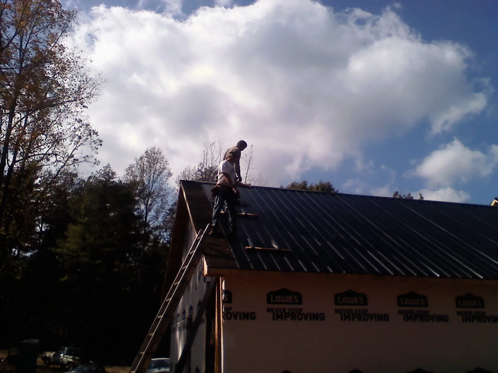 Roofer fastening dark metal panels high against a cloudy sky, from a Roof Inspection job in Broadview